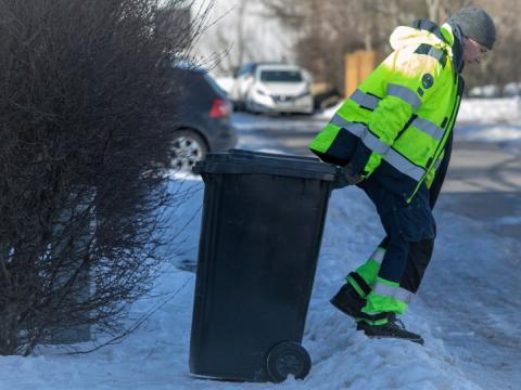 Starfsfólk sorphirðu að draga tunnu yfir snjóruðning