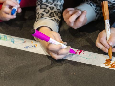 Zbliżenie dziecięcych dłoni rysujących na białym papierze