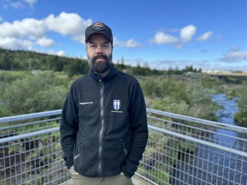 Maður á brú með skóg og á í baksýn.