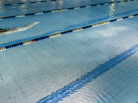 A person swims in a lane at an unspecified swimming pool. The pool is lit, suggesting it's dark outside. The person is in the upper left of the frame.
