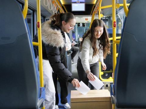 Two tenth-grade girls put ballots in a ballot box on a bus. This was part of the Youth Democracy Festival program