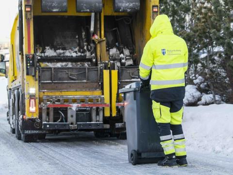 Sorphirðustarfsmaður í gulum galla við tunnu og sorphirðubíl.