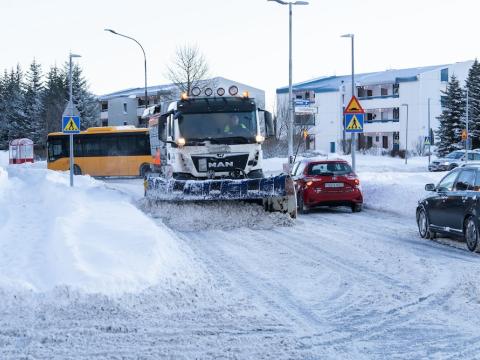 snow plow clearing a street. Snow, houses, and cars nearby.
