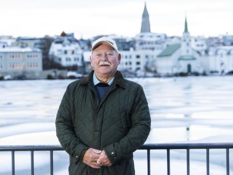 Einar D. G. Gunnlaugsson portrett. Stendur á útsýnispallinum við Tjörnina með tjörn, Fríkirkju og Hallgrímskirkju í baksýn. Vetur, klaki.
