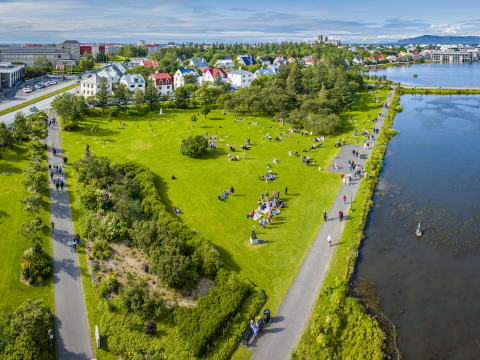 Yfirlitsmynd yfir gras, tré, götur, tjörn og fólk.