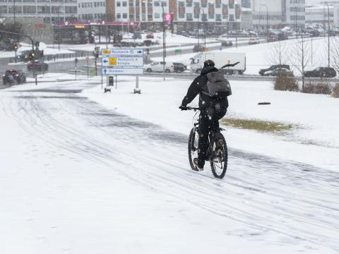 Hjólandi manneskja, snjór á vegi, hús í kring.