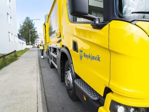 A yellow waste collection vehicle on the street.