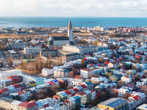 Loftmynd yfir miðborgina, Hallgrímskirkja fyrir miðju, fllugvöllur og sjór í baksýn. Sól.