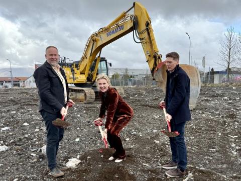 Tveir karlmenn og ein kona taka skóflustungu og bak við þau er grafa