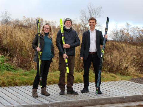 Ásta Briem framkvæmdastjóri Icebike Adventures, Magne Kvam hönnuður skíðagöngubrautanna og Skúli Helgason, formaður menningar- og íþróttaráðs Reykjavíkur stilltu sér upp eftir að hafa skrifað undir samning um gönguskíðaspor, við Rauðavatn. Standa með gönguskíði, gróður í kringum þau.