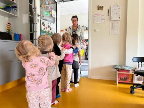 Preschool children in a line with a teacher greeting them