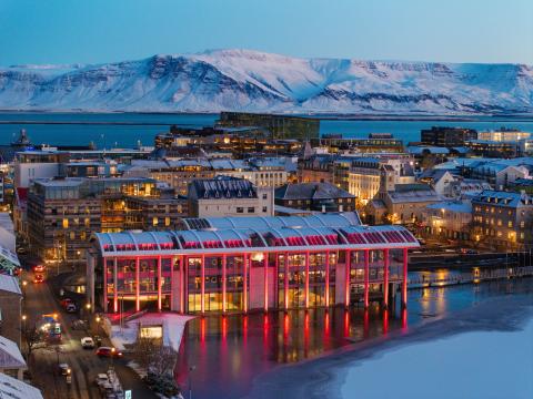 Ráðhúsið lýst rautt í forgrunni, í bakgrunni Miðborgin og Esjan. Skuggsýnt, desember.