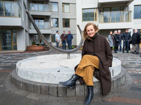Anna Júlía Friðbjörnsdóttir við verk sitt Rif í Vesturvin. Situr á verkinu, fólk í baksýn sem var við vígslu á verkinu.