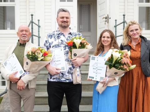 Three individuals holding flowers stand alongside the mayor.