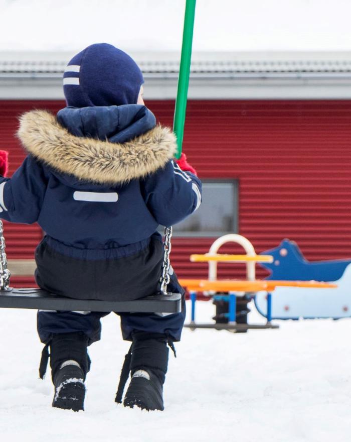 Barn í dökkbláum útigalla með húfu að róla sér á leikskólanum Álftaborg