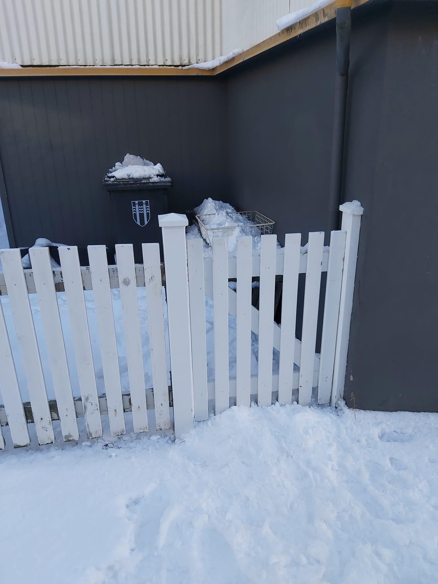 Sorptunna í snjó á bakvið grindverk.