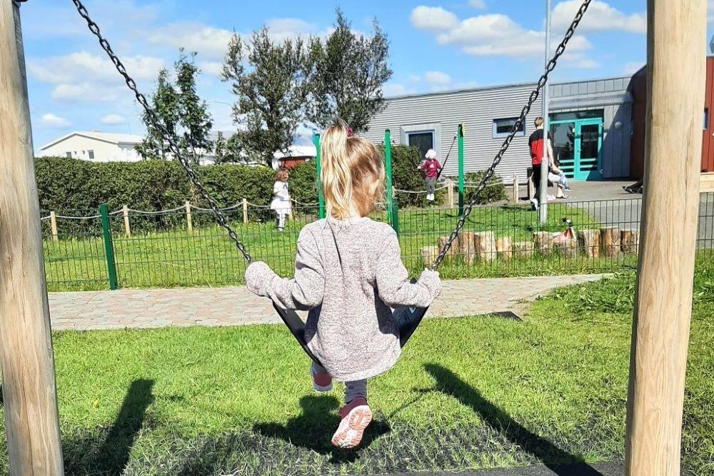Stúlka að róla sér að sumri til á leiksvæði leikskólans Lyngheima