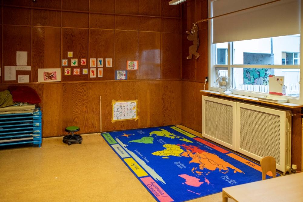Panel wall displaying children's artwork and colorful rug with world map at Miðborg Preschool-Barónsstígur