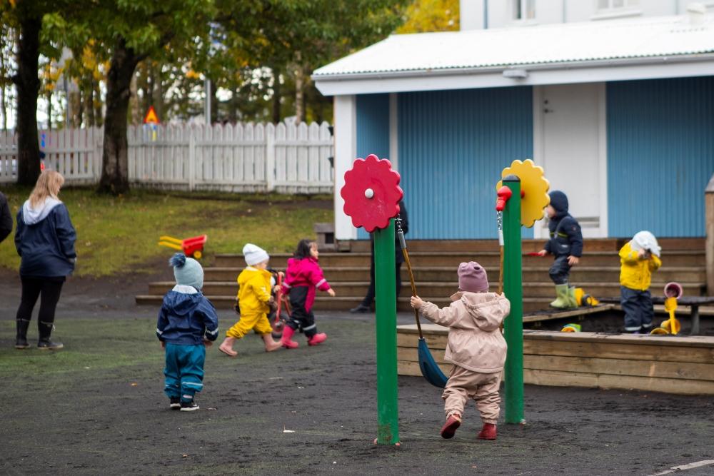 Children playing in colorful outdoor overalls on the playground at Miðborg Preschool on Barónsstígur