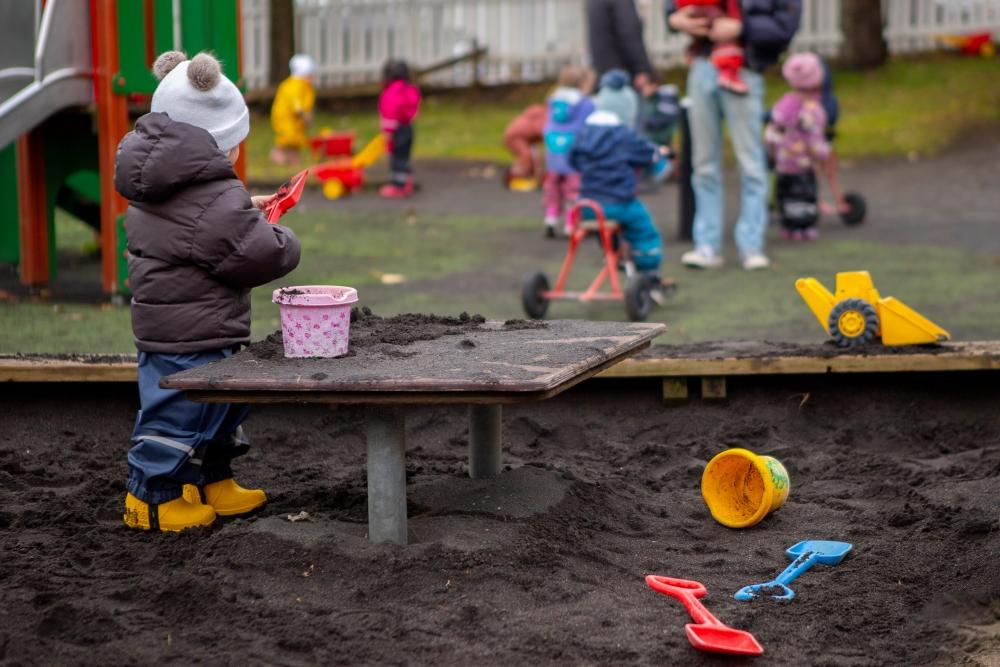 Child playing with shovel and bucket in sandbox at Miðborg Preschool, Barónsstígur. More children in the background.