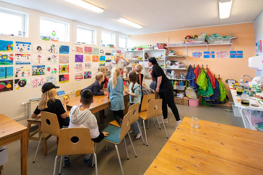 Börn sitja við borð og hlusta á leiðbeinanda á frístundaheimilinu Glaðheimum