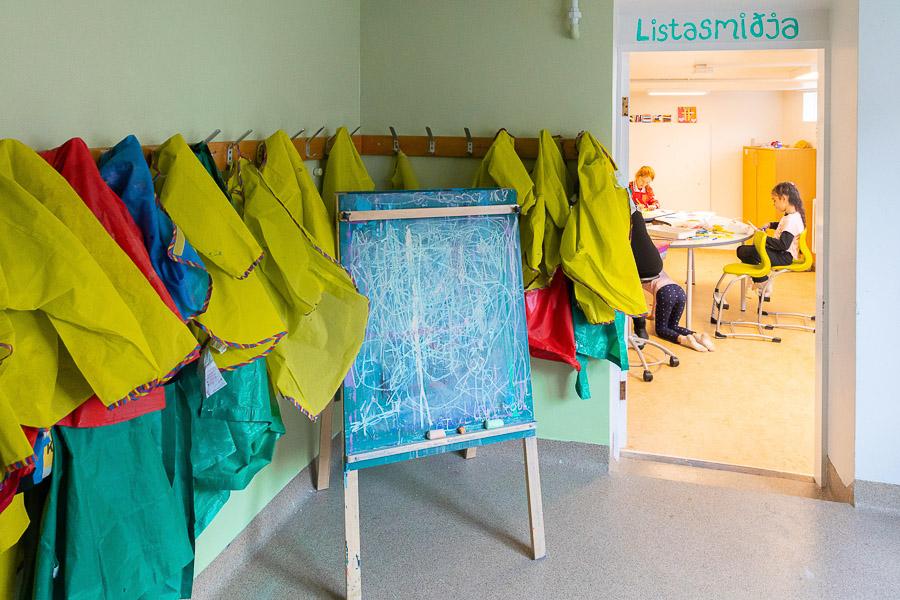 Dyraop með yfirskriftinni Listasmiðja, trönur og vesti til að verja föt fyrir málningaslettum hangandi á vegg. 
