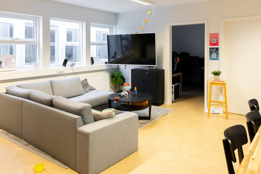 Light corner sofa, small table and TV screen. Chairs to the side.