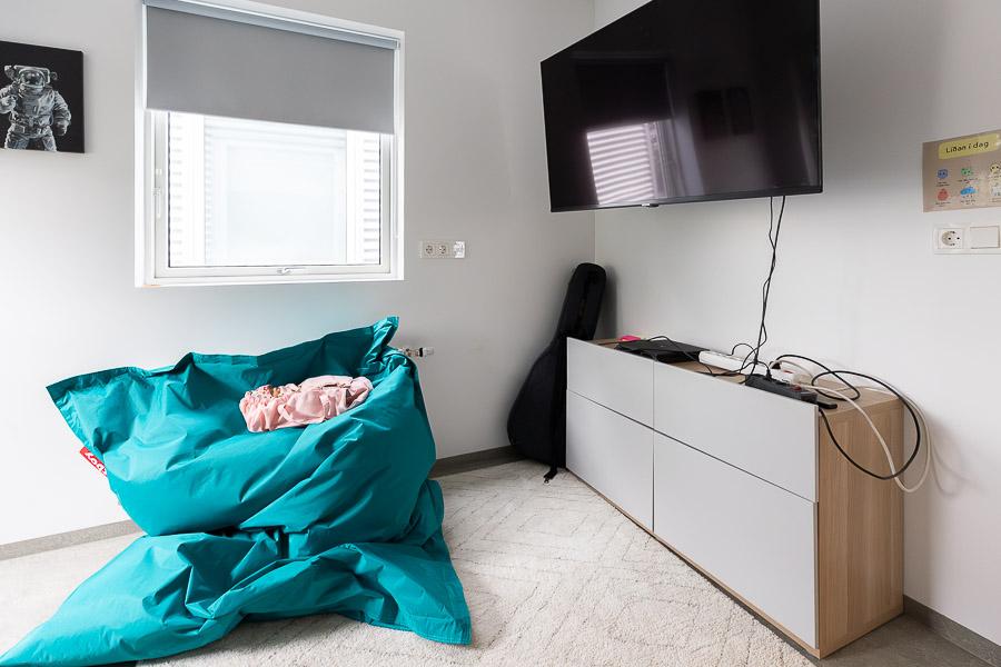 Corner area with blue bean bag, shelf and large screen.