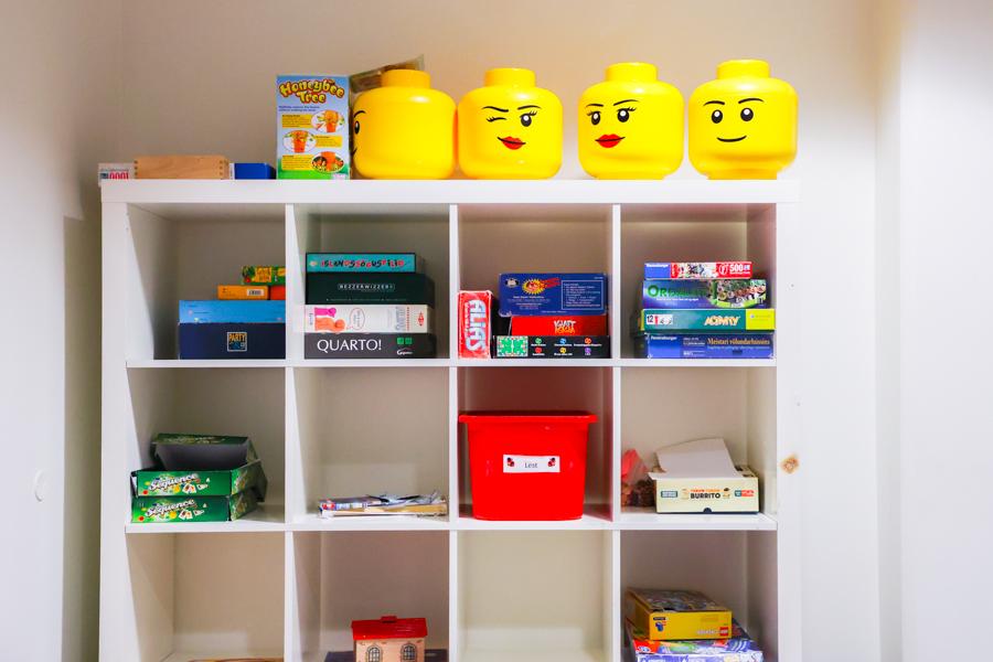 Shelf containing various board games with large Lego figure heads displayed on the top shelf.