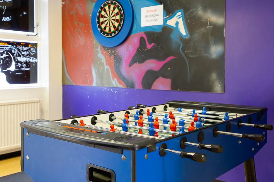 Room with a foosball table and dartboard on the wall. Wall decorated with artwork. 