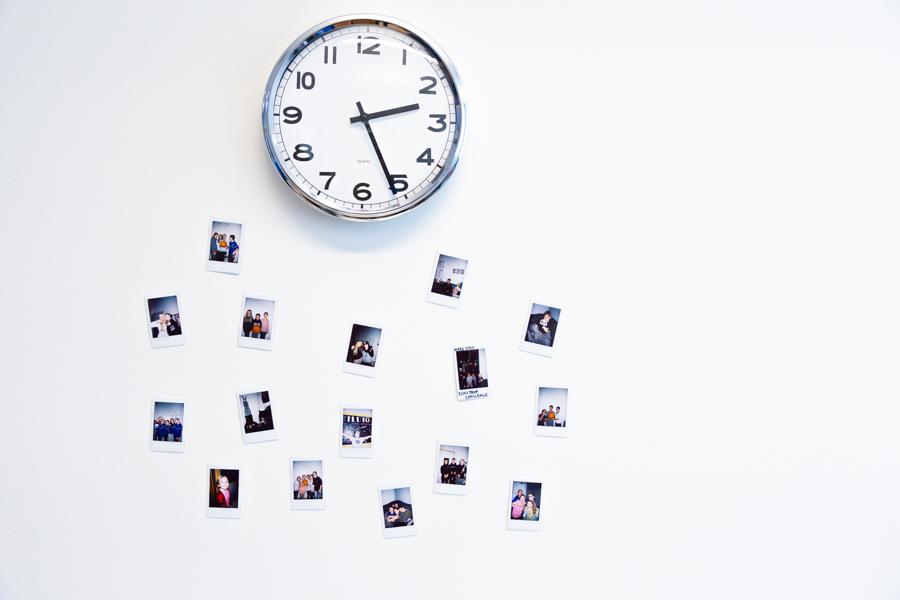 Clock on a white wall. Below the clock are Polaroid pictures of young people.