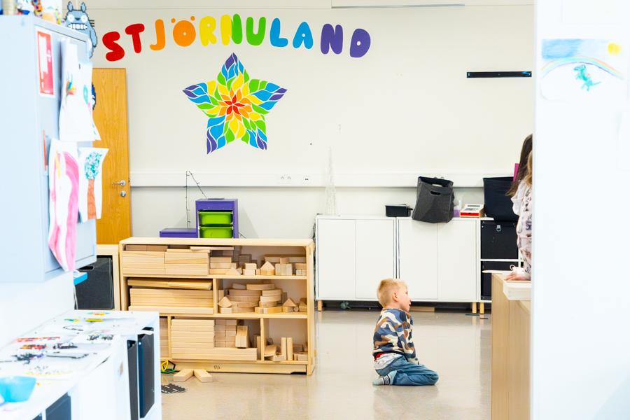 Barn situr á gólfi í leikherbergi. Hillur til hliðar með stórum trékubbum. Á vegg er stór stjarna og marglitir starfir sem mynda orðið Stjörnuland. 