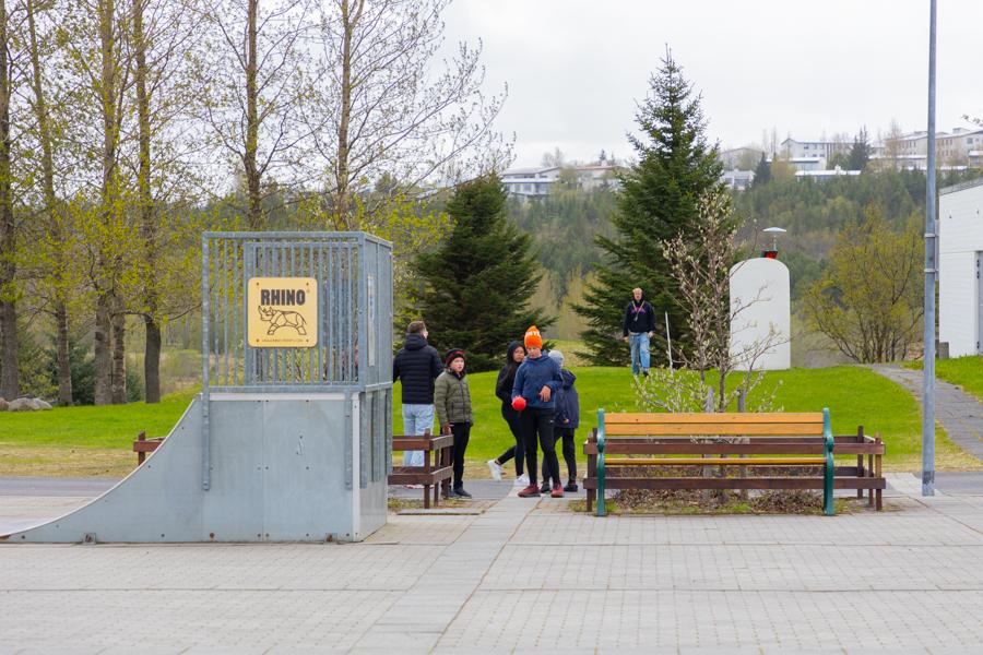 Börn á útileikvelli. Hjólabrettarampur og bekkir. 