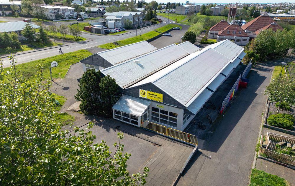 Aerial view of the long building housing Hólmasel youth center. Green leaves in foreground. 