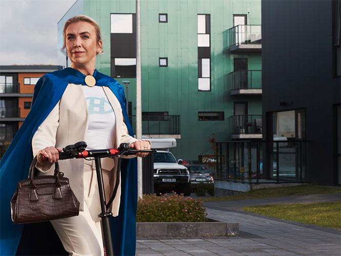 A woman in a cape riding a scooter, promotional image for My Neighborhood.