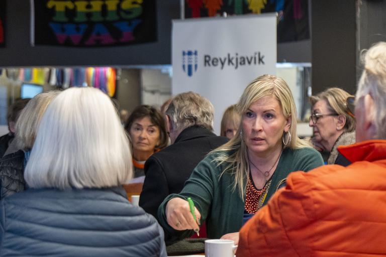 Fólk á íbúafundi Miðborgar í Spennistöðinni. Ein kona forgrunni, í bakgrunni sést merki borgarinnar á tjaldi
