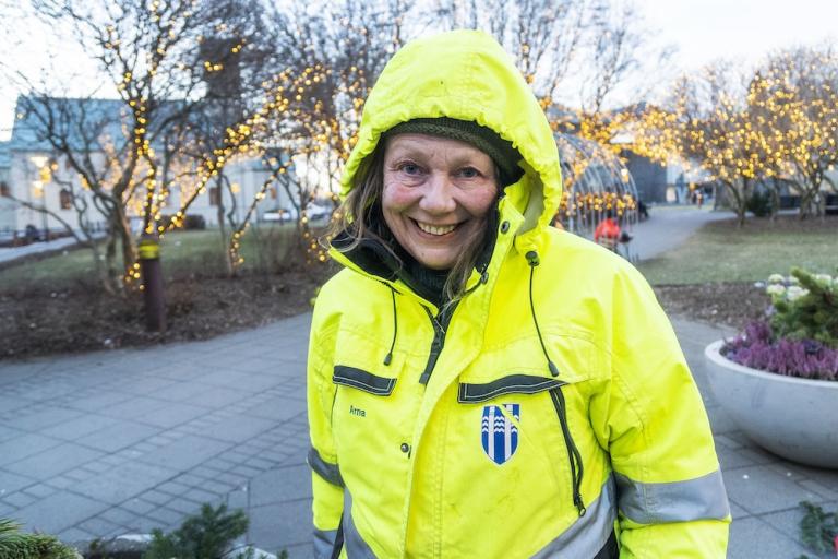 Kona í úlpu. Á bak við hana eru blóm og tré með jólaljósum.