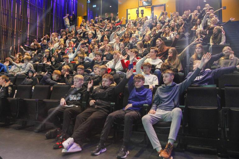 Young people at the Youth Democracy Festival in Harpa. They sit in a hall with hands raised to vote between issues.