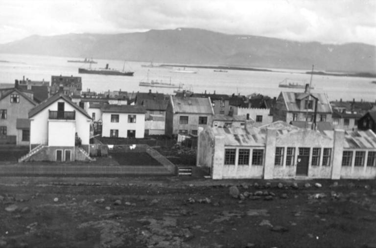 Svarthvít mynd tekin úr braggahverfinu á Skólavörðuholti. Listvinahús Guðmundar frá Miðdal hægra megin í ramma, herskip á Faxaflóa og Esjan í fjarska.