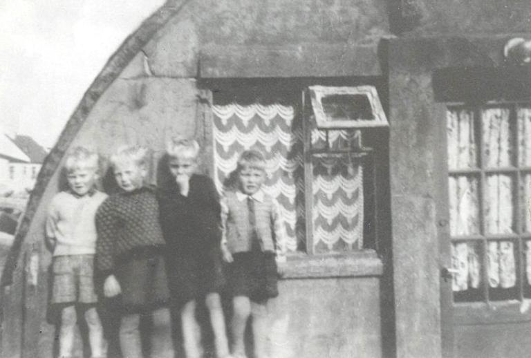 Svarthvít mynd úr braggahverfinu á Skólavörðuholti. Fjórir drengir, sirka sjö ára, standa framan við bragga.