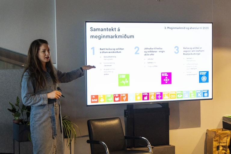 Harpa Þorsteinsdóttir, project manager for Public Health Affairs at the Office of the Mayor and Chief Executive Officer, presents findings on the Health and Well-being of LGBT+ People in the "Pool" area of City Hall. Standing by a screen and pointing to data