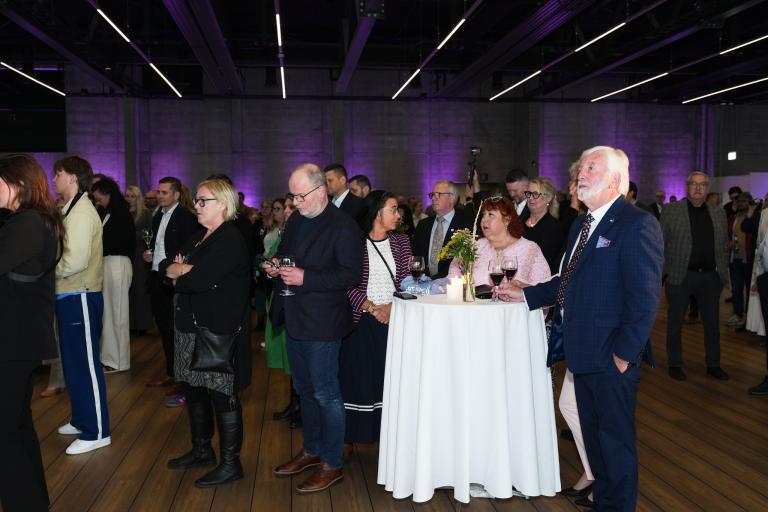 A group of guests in the softly lit event hall of the Vör passenger terminal. A table with a white tablecloth at the center, surrounded by guests.