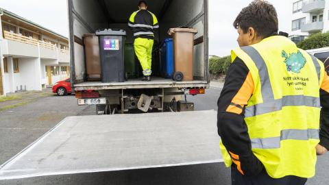 Truck with waste bins and people working on the bin swap.