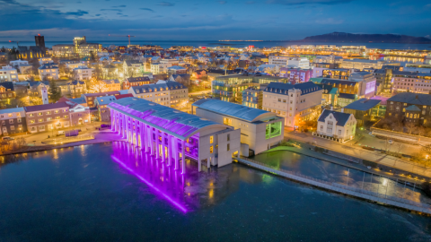 Ráðhús Reykjavíkur um vetur úr lofti lýst fjólubláum ljósum. Einnig sést Kvosin úr lofti.