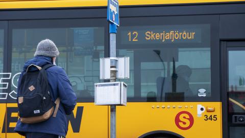 maður sem stendur fyrir utan strætisvagn, strætóskilti til hliðar.