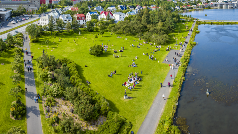 Yfirlitsmynd yfir gras, tré, götur, tjörn og fólk.