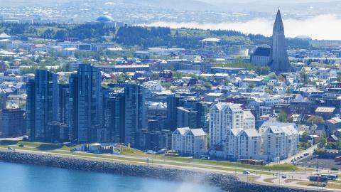 Loftmynd yfir Reykjavík, útsýni frá Sæbraut, yfir miðborg, að Hallrímskirkju og Perlu. Sjór í forgrunni, fjöll og sjór í bakgrunni. Mistur yfir.