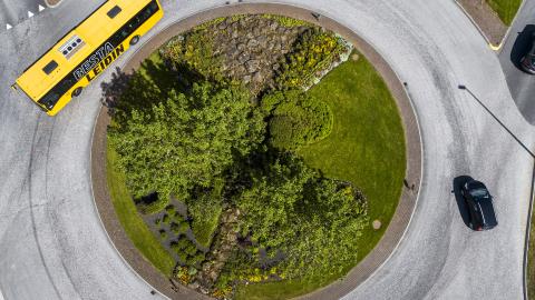 Loftmynd af Strætó að keyra í kringum gróðursælt hringtorg.