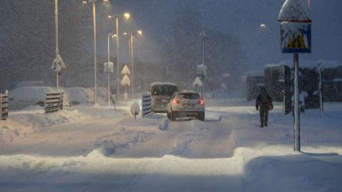 Bíl á götu með miklum snjó og ein manneskja á gangi