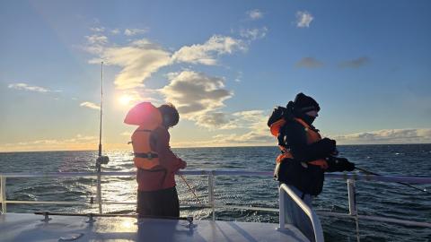 Two kids in life jackets with fishing rods while fishing out at sea.